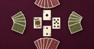 Four fans of playing cards surround a central spade trick on a plum-coloured table, with matching card backs marking opposite partnerships.