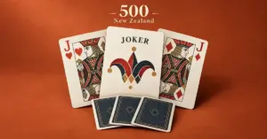 A joker flanked by the jacks of hearts and diamonds sits above three face-down kitty cards on a terracotta background, beneath the words “500 New Zealand”.