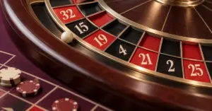 A close-up of a roulette wheel with red and black numbered pockets, an ivory ball and chips on a plum-coloured betting table.