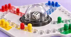 Close-up of a Trouble board with a die inside the clear Pop-O-Matic dome and red, yellow, green and blue playing pegs.
